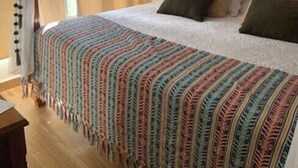 Een slaapkamer met een gestoffeerd hoofdeinde, een kleurrijk gestreept dekbed en een baldakijnbed.