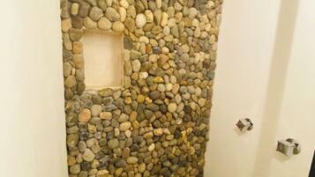 Un bagno con una parete in pietra, una piccola finestra quadrata e un pavimento piastrellato.