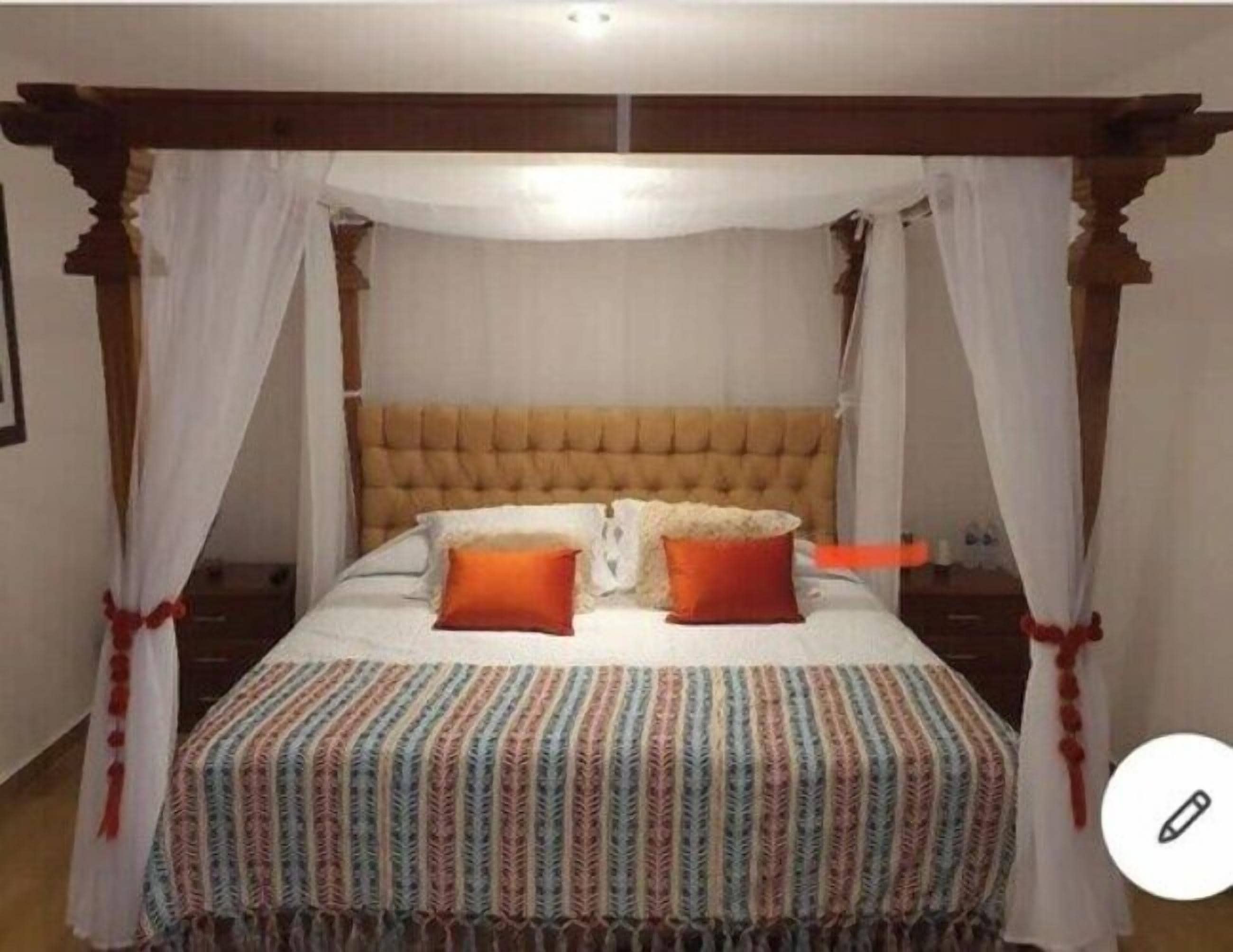 A four-poster canopy bed with a tufted headboard, white bedding, and a colorful striped blanket.