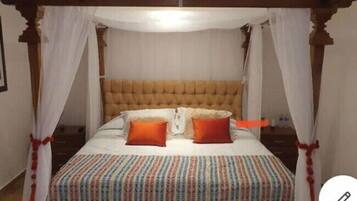 A four-poster canopy bed with a tufted headboard, white bedding, and a colorful striped blanket.