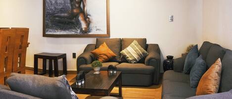 A living room with a sofa, armchairs, a coffee table, and a painting on the wall.