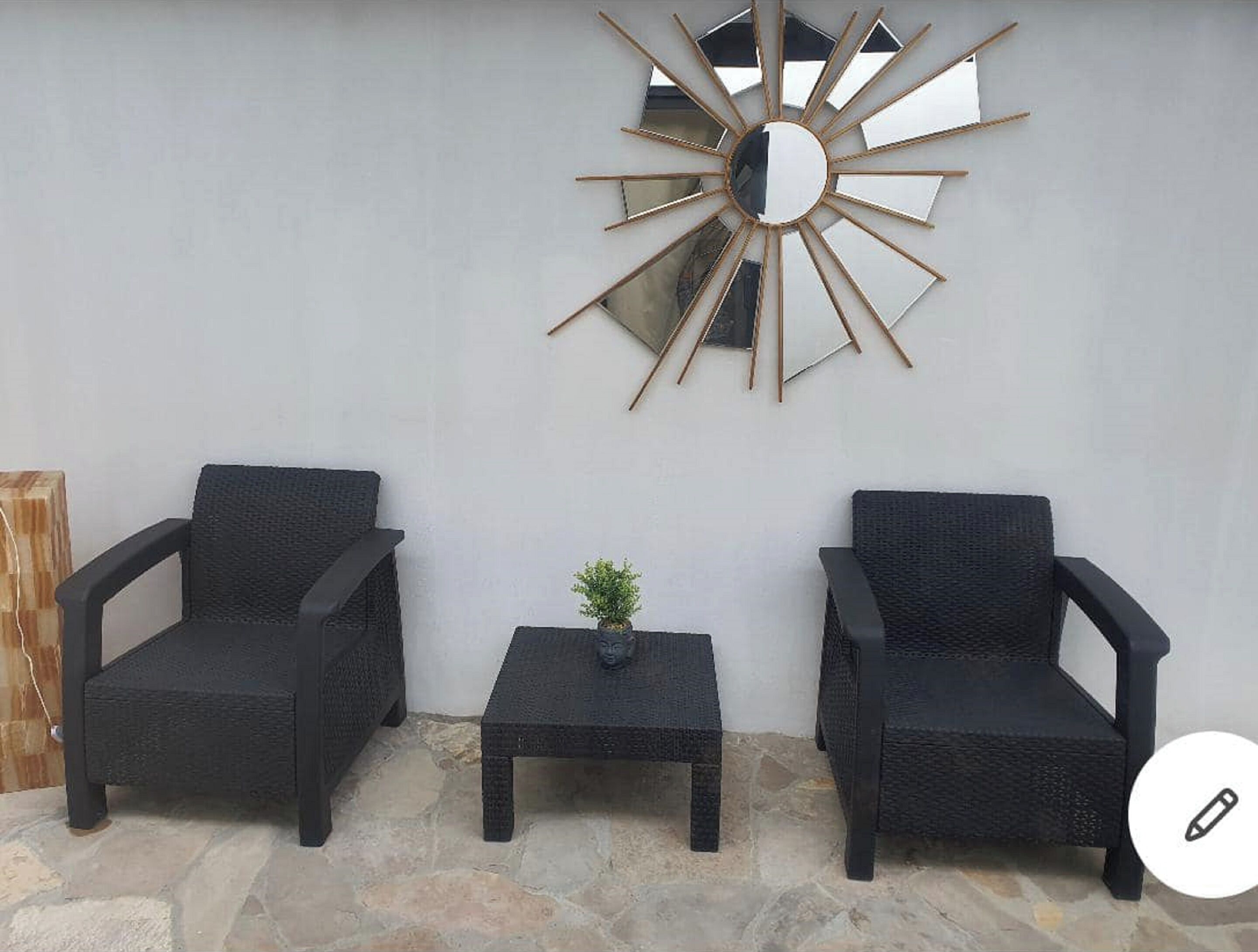 Two black wicker chairs, a small table, and a wall-mounted mirror with a sunburst design.