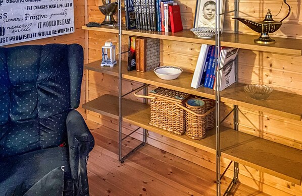 A cozy room with a wooden floor, a blue polka dot chair, a bookshelf with books and a framed photo, and a metal shelf with baskets and a lantern.