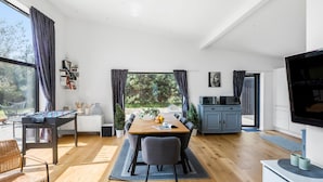 Una sala moderna con una mesa de comedor de madera, sillas grises, una mesa de fútbol y un televisor a la derecha.