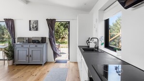 Una cocina moderna con encimera negra, un lavamanos y una ventana. Se observa un mueble con microondas y una planta.