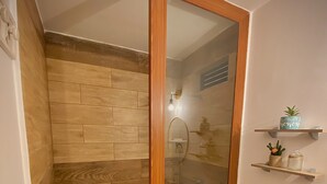 Un baño con pared de madera, cabina de ducha de vidrio, inodoro y estante con adornos.