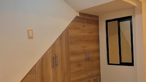Una habitación con un armario de madera, un ventanal pequeño y una lámpara en el techo.