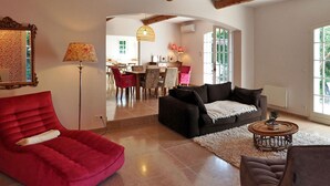 A spacious living room with a red armchair, a black sofa, and a dining area in the background. - Les Lauriers De Fontvieille (Fonvieille)