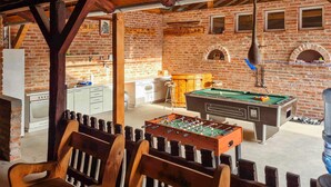 Un espace intérieur accueillant, doté d’un baby-foot, d’une table de billard et d’un coin cuisine avec un mur en briques et des poutres en bois.