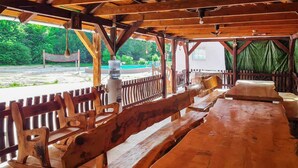 Un pavillon extérieur en bois, doté de bancs et d’une table, entouré d’une clôture en bois, et offrant une vue sur une piscine et un espace verdoyant.