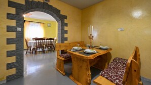 Un coin repas avec une table en bois dressée pour quatre personnes, un banc agrémenté d’un coussin à motifs et un chandelier avec des bougies.