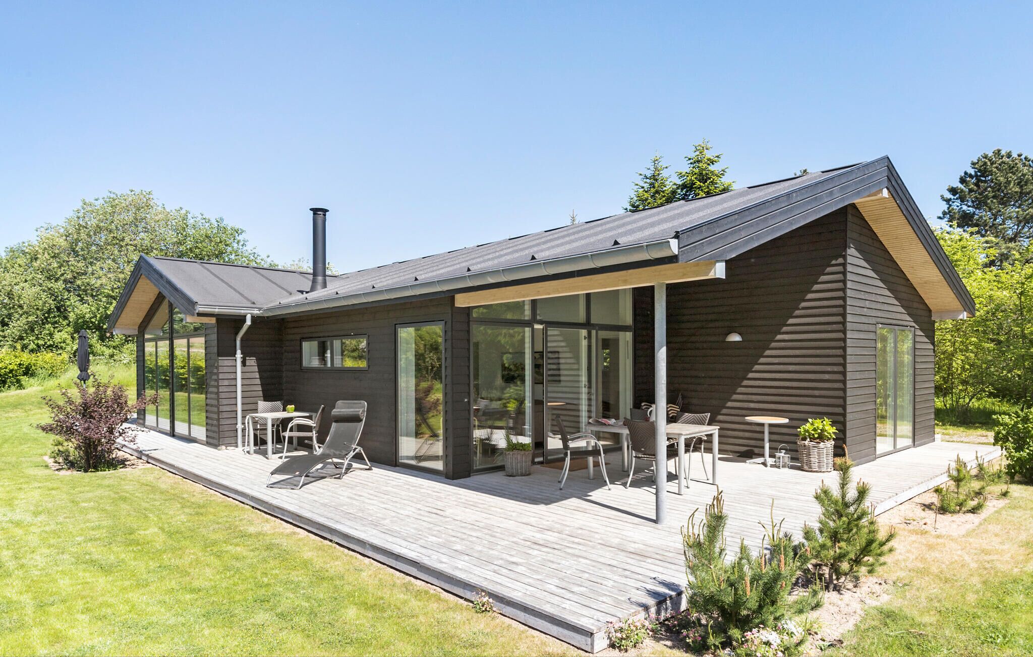 A modern cabin with a deck, large windows, and a chimney.