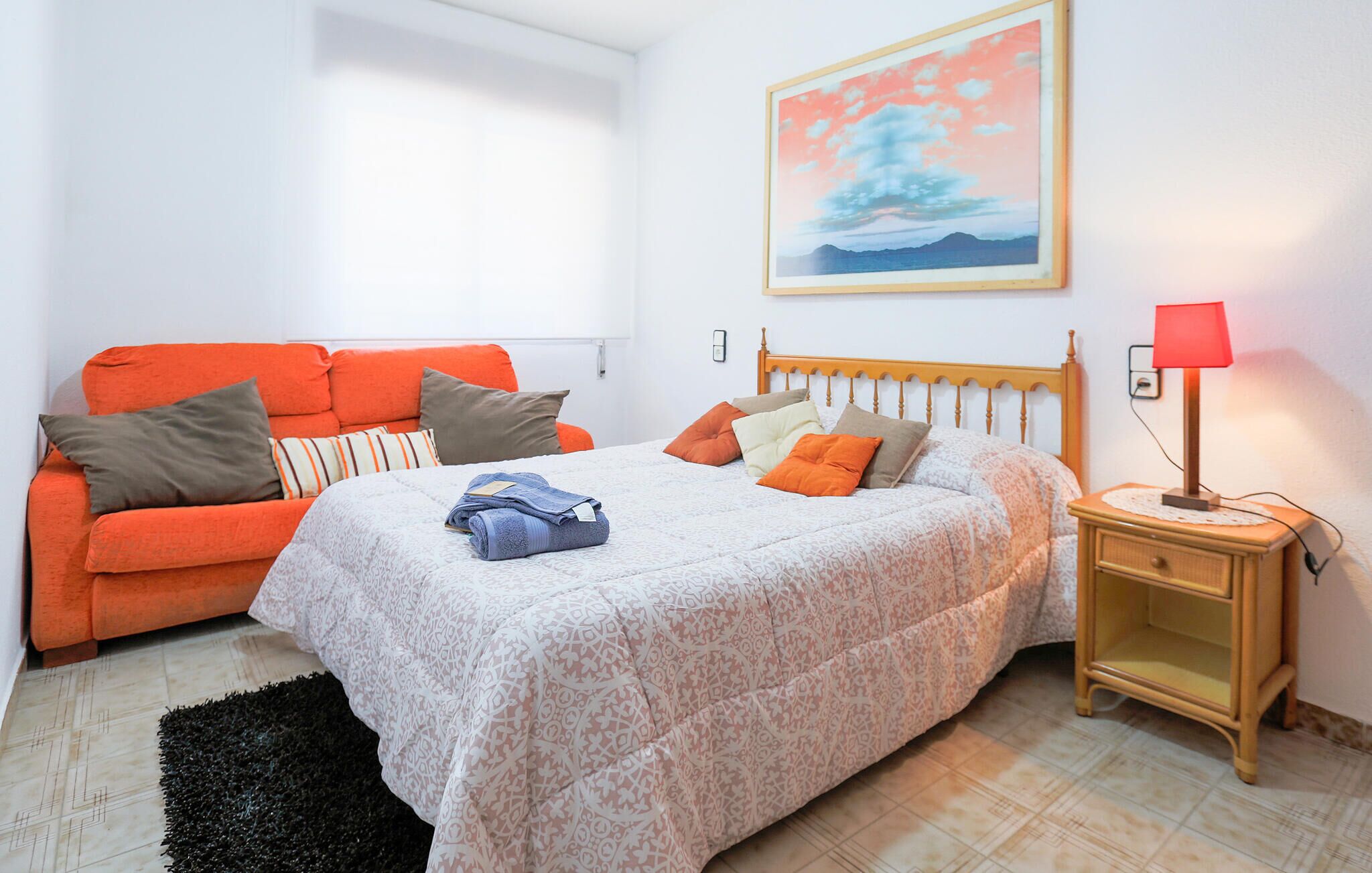 Ein Schlafzimmer mit einem Bett, einem orangefarbenen Sofa und einem Nachttisch mit einer Lampe.