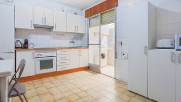 Une cuisine avec des meubles blancs, une cuisinière, un four à micro-ondes et un lave-linge.