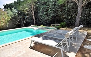 Ein Swimmingpool mit weißer Liegefläche, Liegestühlen und einer Schaukel.