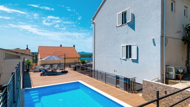 Una piscina con muelle de madera, sillas de descanso y vistas al mar.
