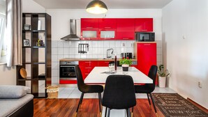 Una cocina compacta con armarios rojos, un microondas y un comedor con una mesa blanca y sillas negras.