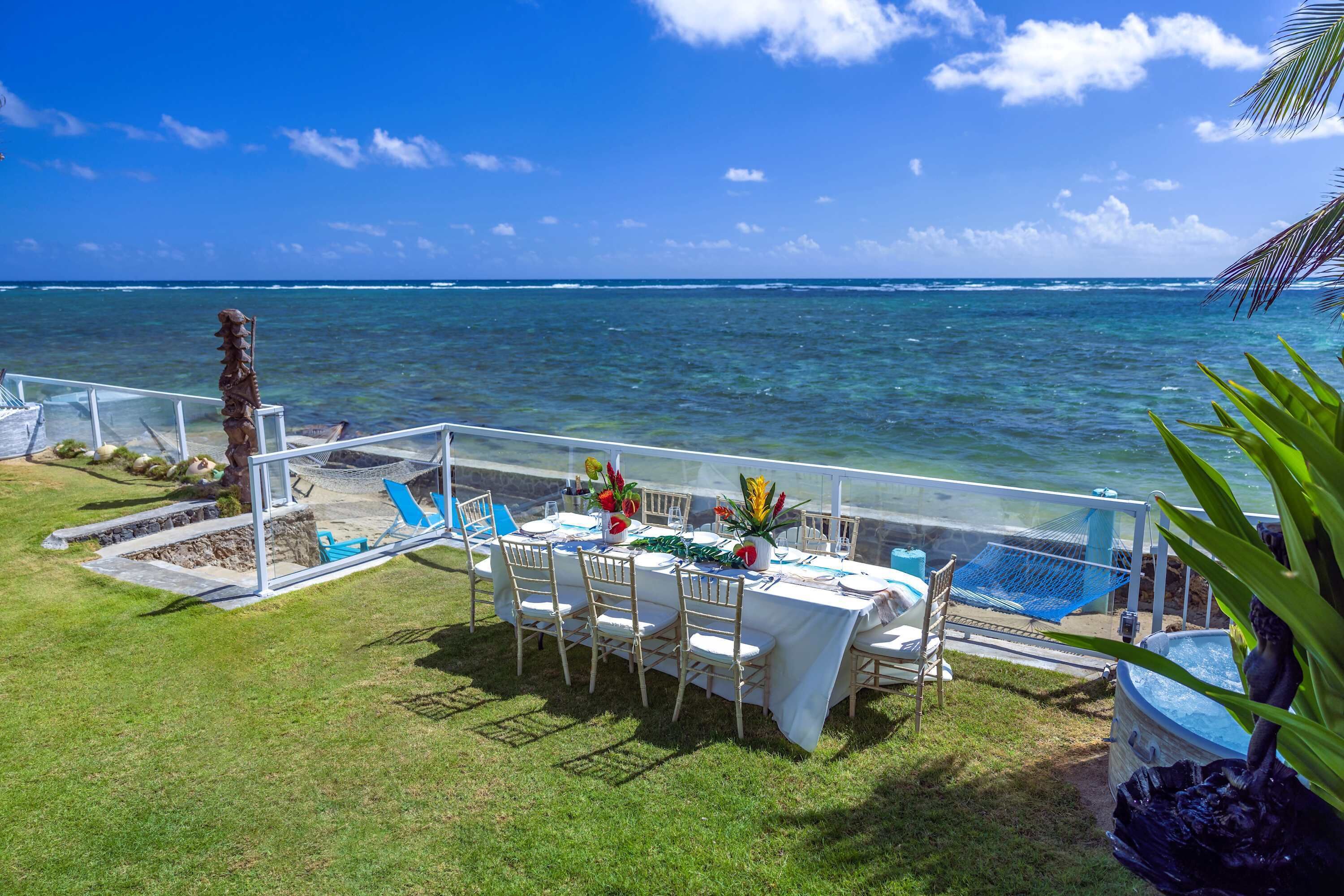 An outdoor dining area with a view of the ocean, a hot tub, and a poolside chair.