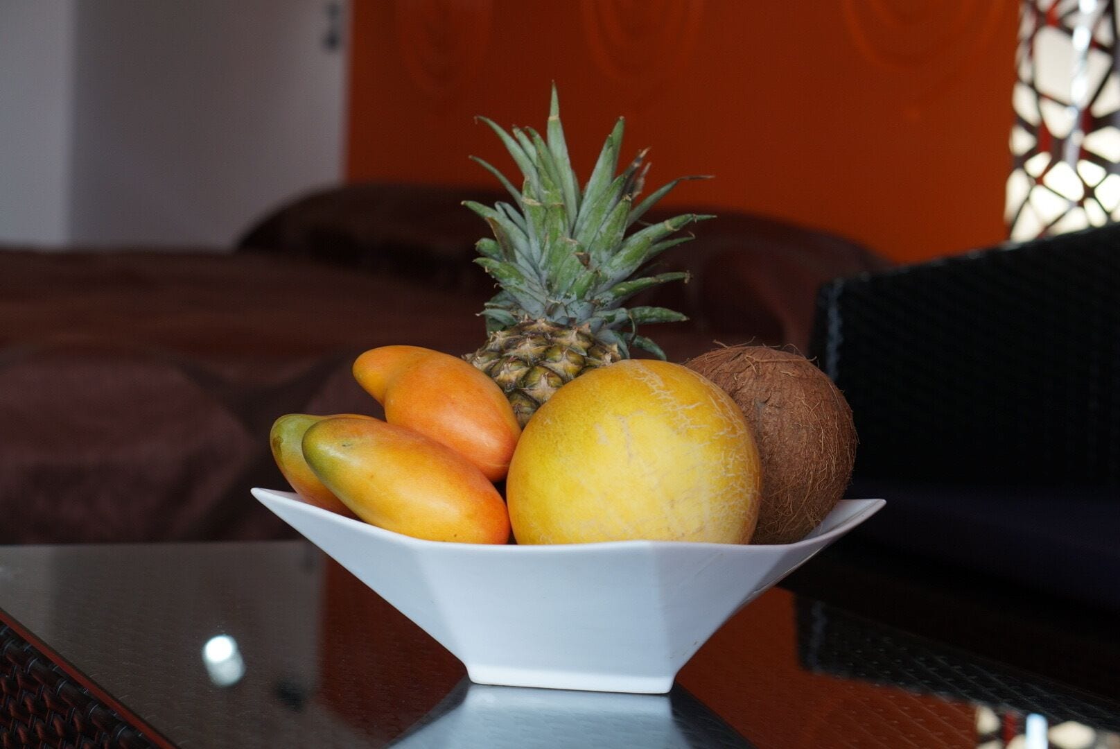 Un tazón de fruta sobre una mesa, con una cama al fondo.