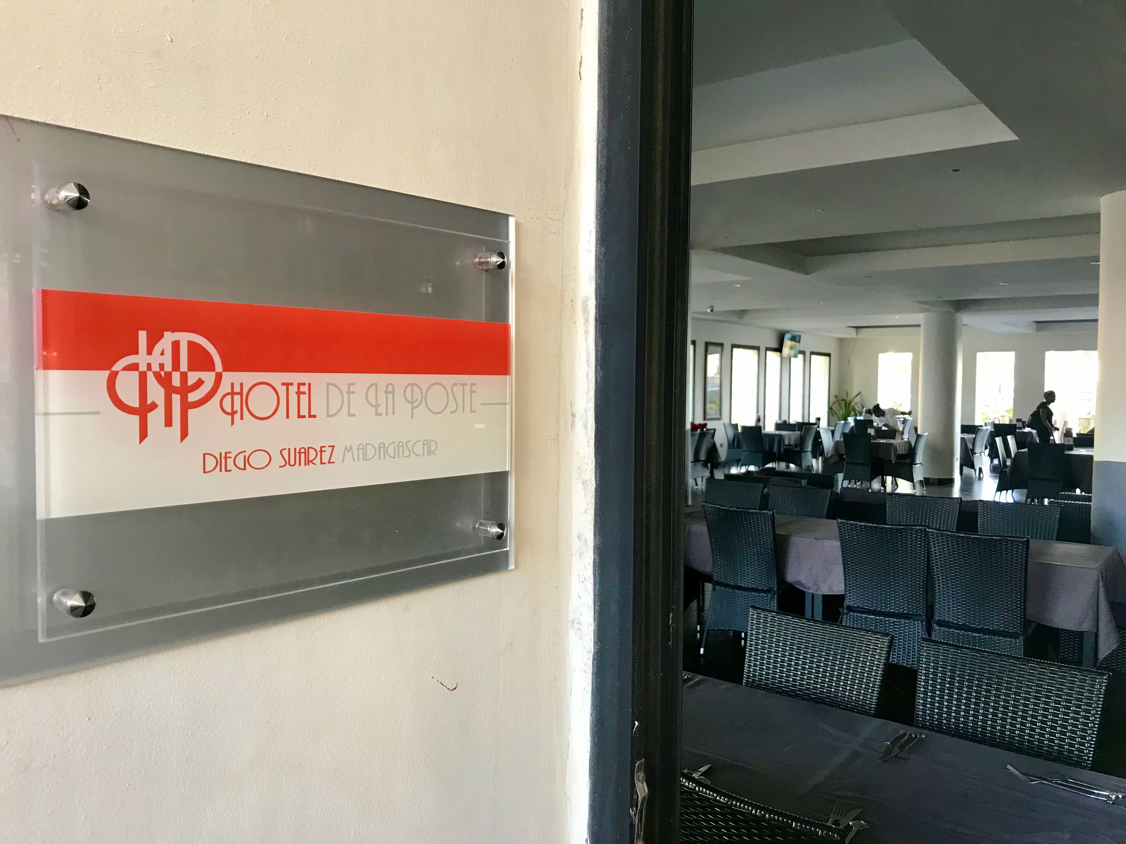 Un letrero de hotel con un logotipo rojo y blanco, y una vista del comedor con mesas y sillas.