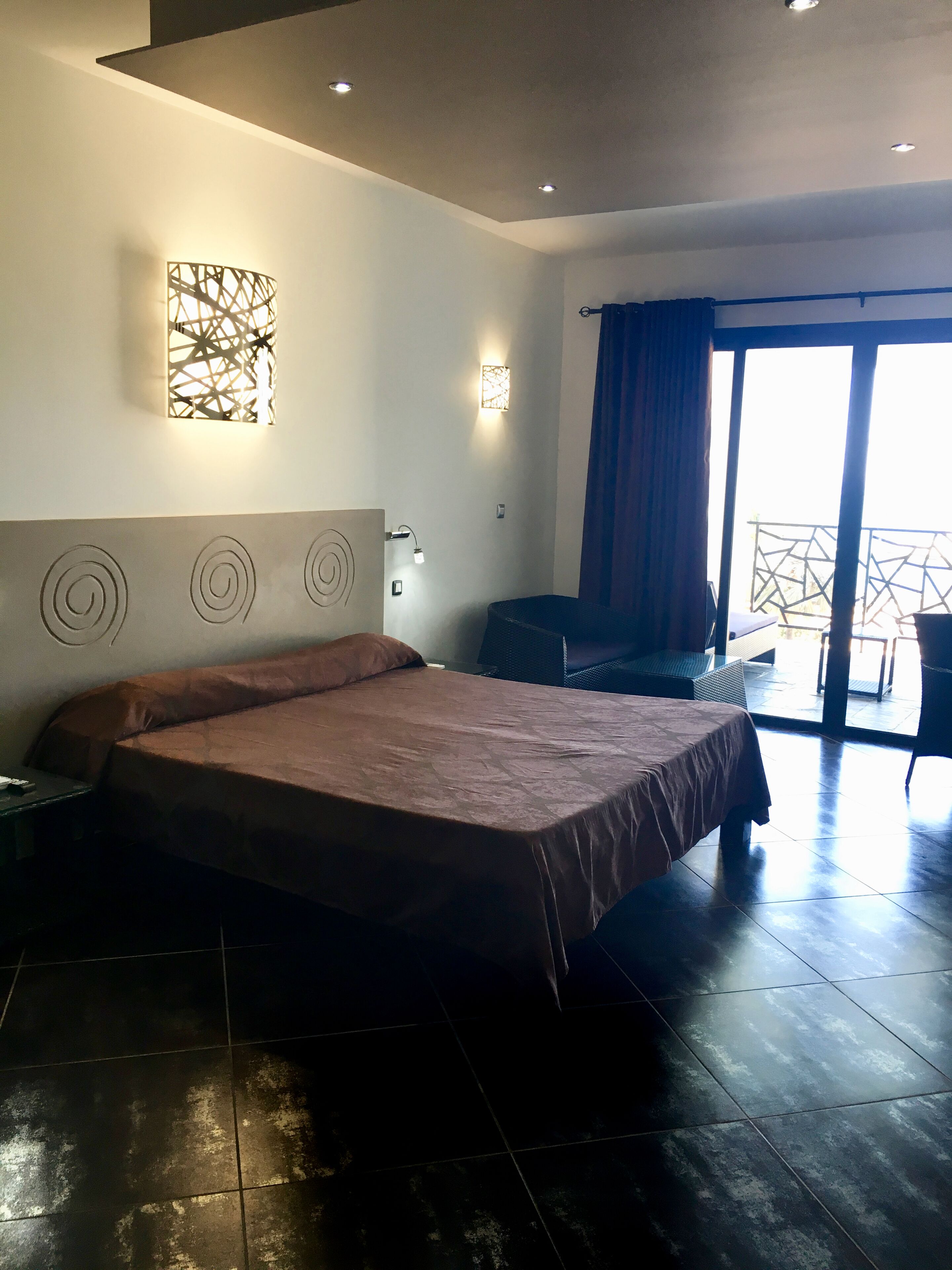 A modern hotel room with a large bed, a desk, and a balcony with a view.