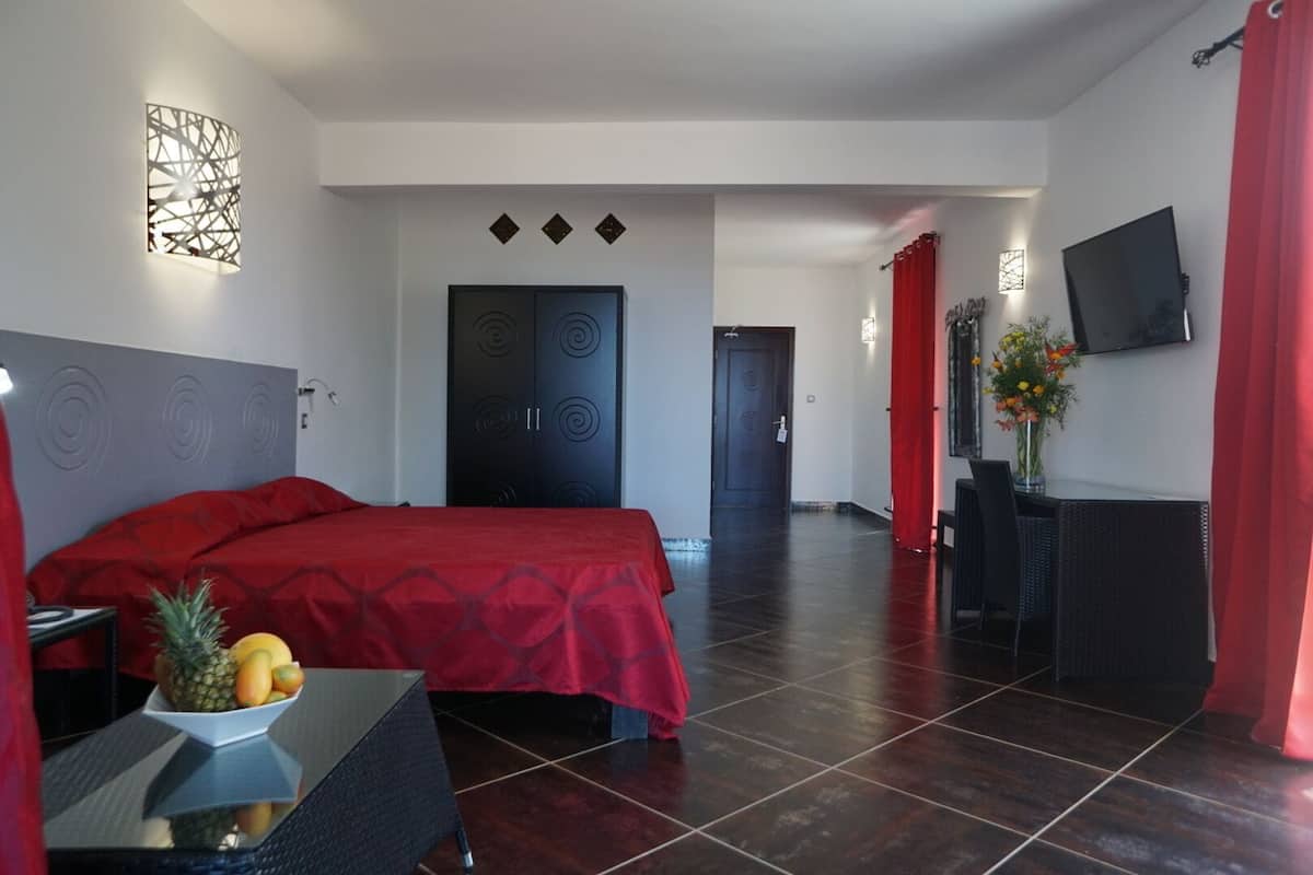 Een hotelkamer met een bed, een bureau met een schaal fruit, een televisie en een rood gordijn.