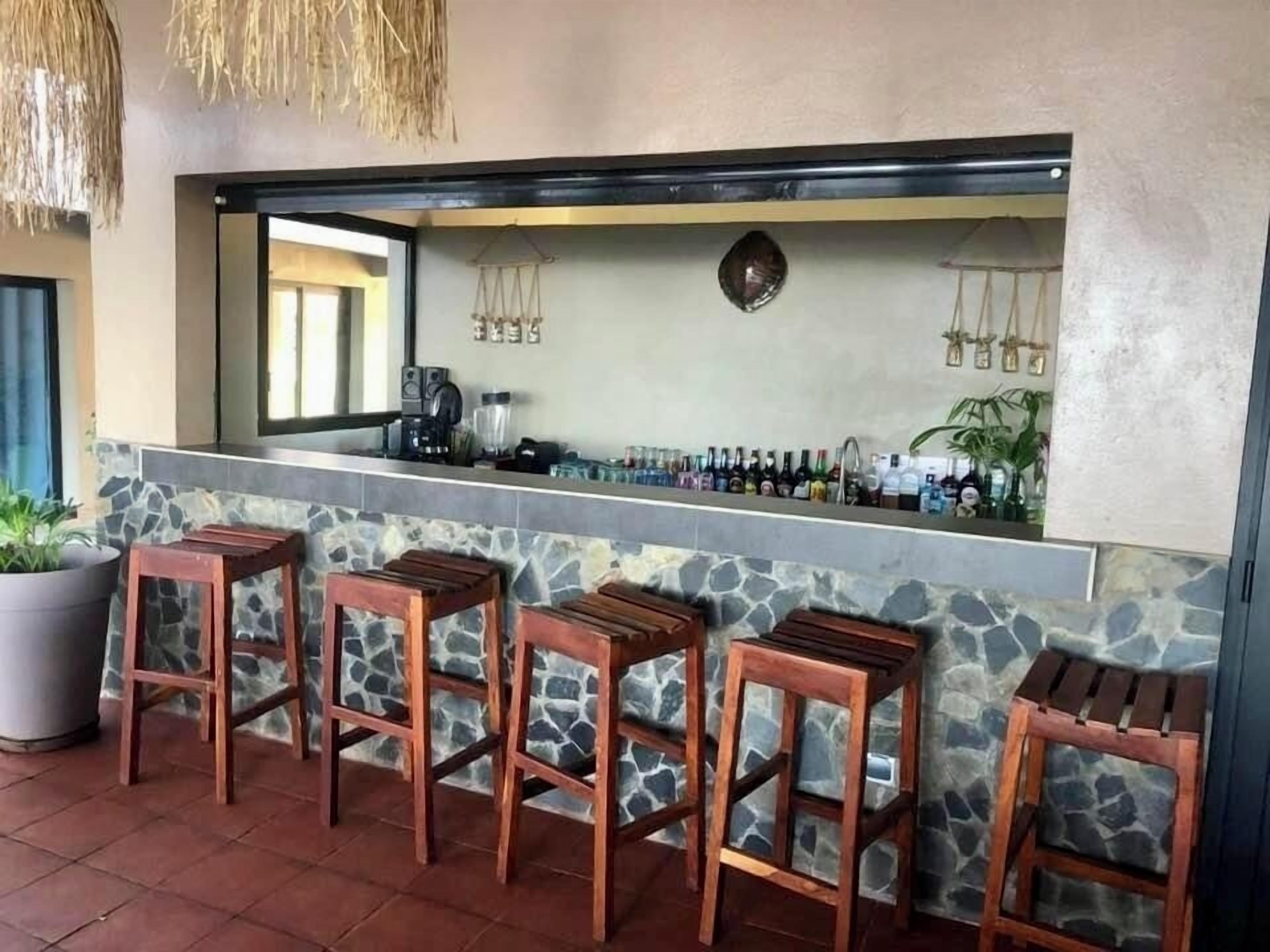 Zona de bar con detalles de piedra, taburetes de madera y una variedad de botellas.