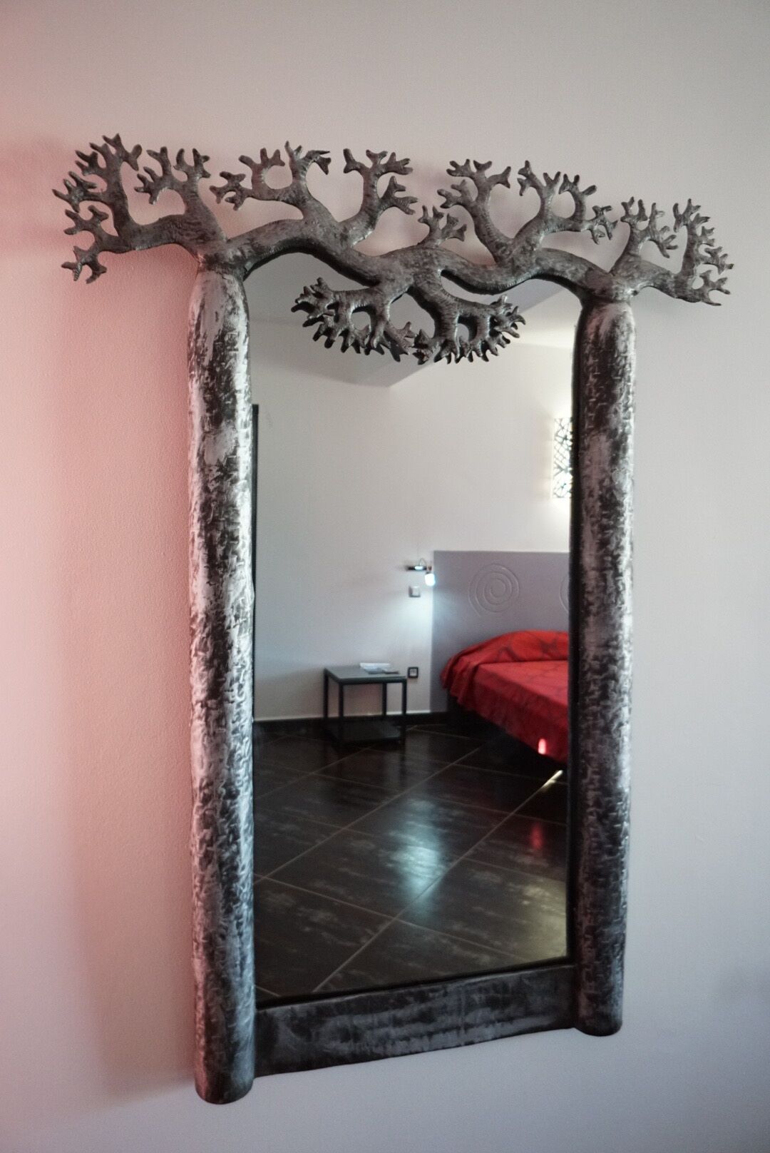 Un espejo con un marco similar a un árbol en una habitación con una cama y una mesita.