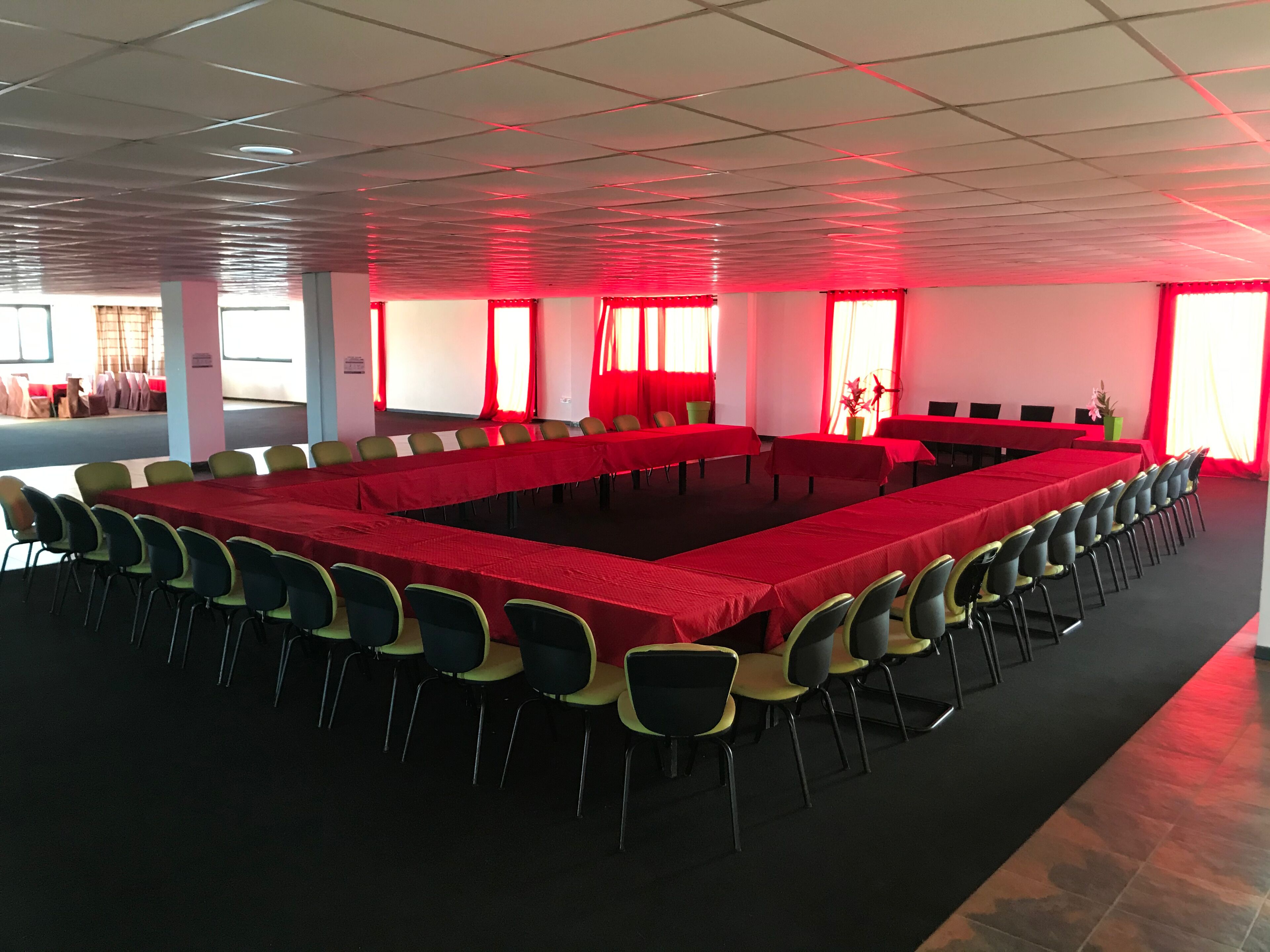 A conference room with a long table and chairs, large windows with red curtains, and a tiled ceiling.