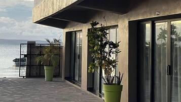 Un bâtiment moderne avec une façade en béton, de grandes fenêtres et un balcon donnant sur une étendue d’eau.