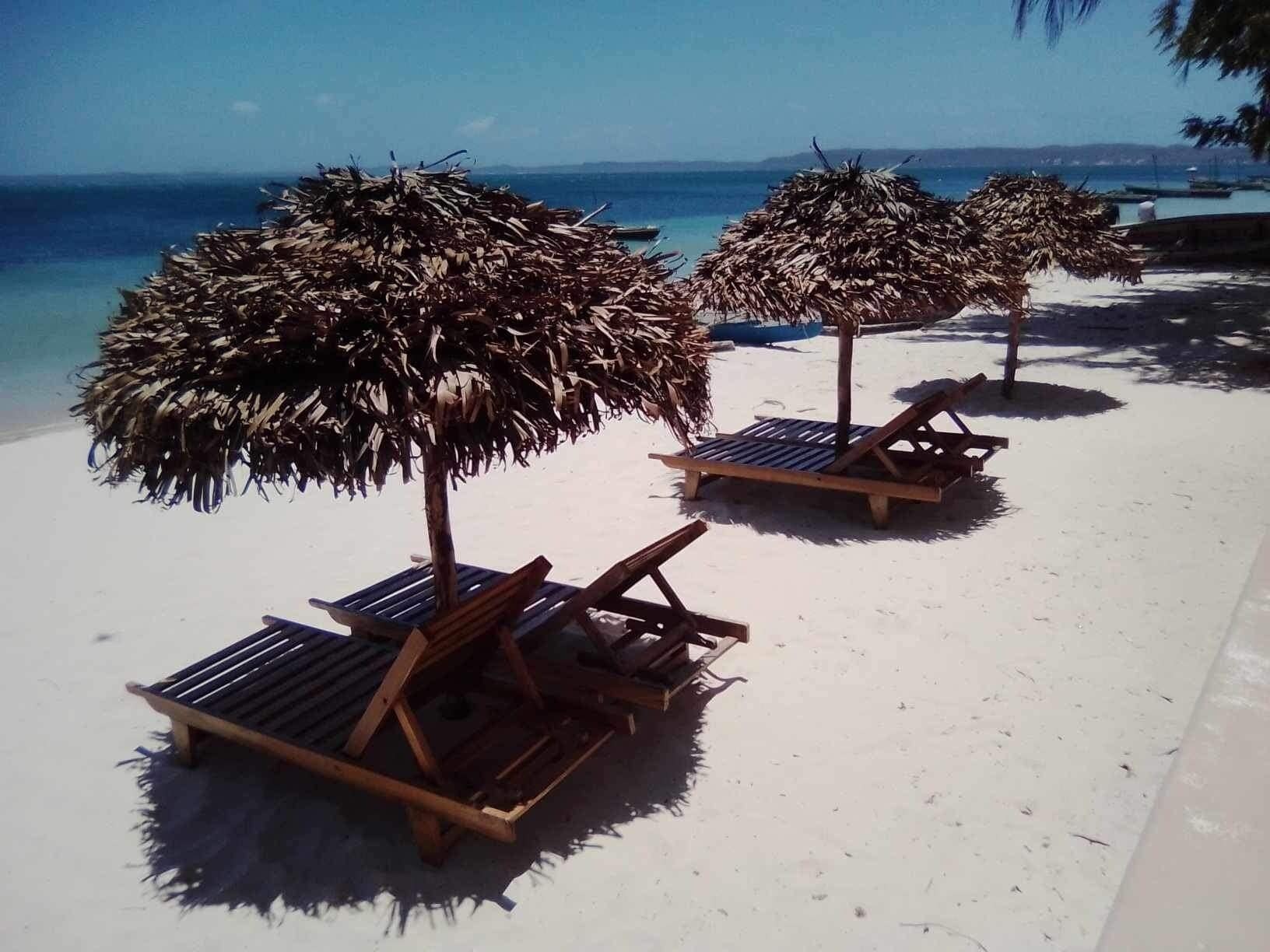 A beach with wooden lounge chairs and thatched umbrellas.