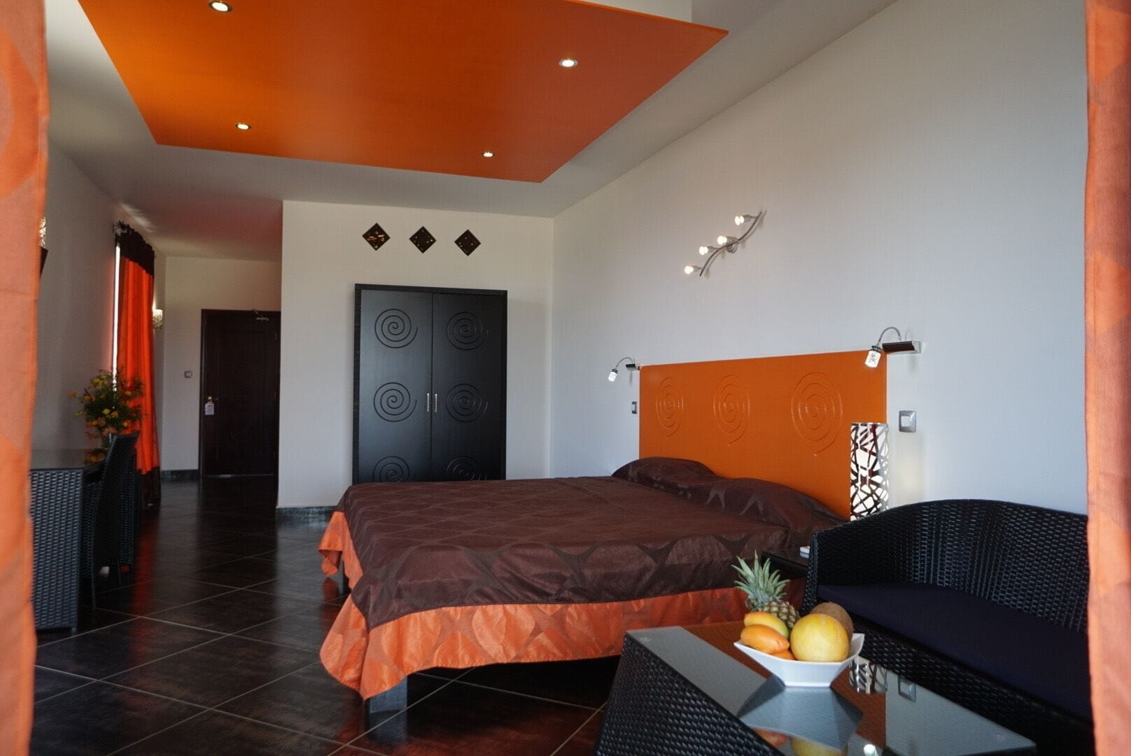 A modern hotel room with a large bed, a dining area, and a fruit bowl on the table.