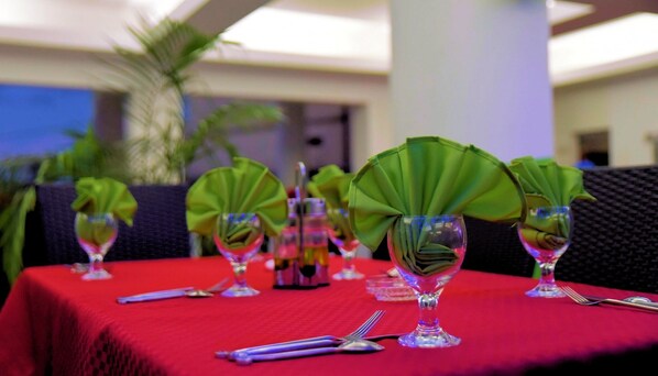 Una mesa con ventiladores verdes, vasos transparentes y cubiertos sobre un mantel rojo.