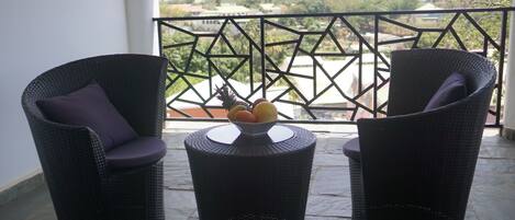 Un balcón con sillas de mimbre y una pequeña mesa redonda con un frutero.