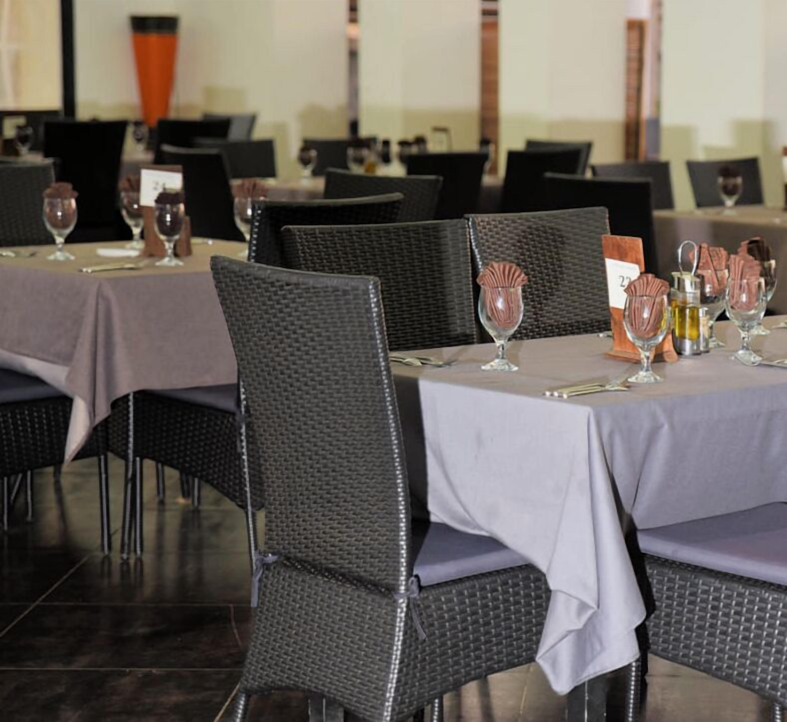 A restaurant with tables set for dining, featuring dark woven chairs and light tablecloths.