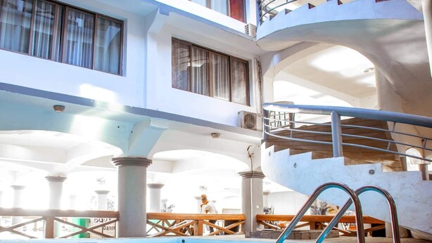 A hotel pool area with a clear view of the pool, a staircase, and a lounge area with wooden furniture. - Hotel de la Poste (Antsiranana)