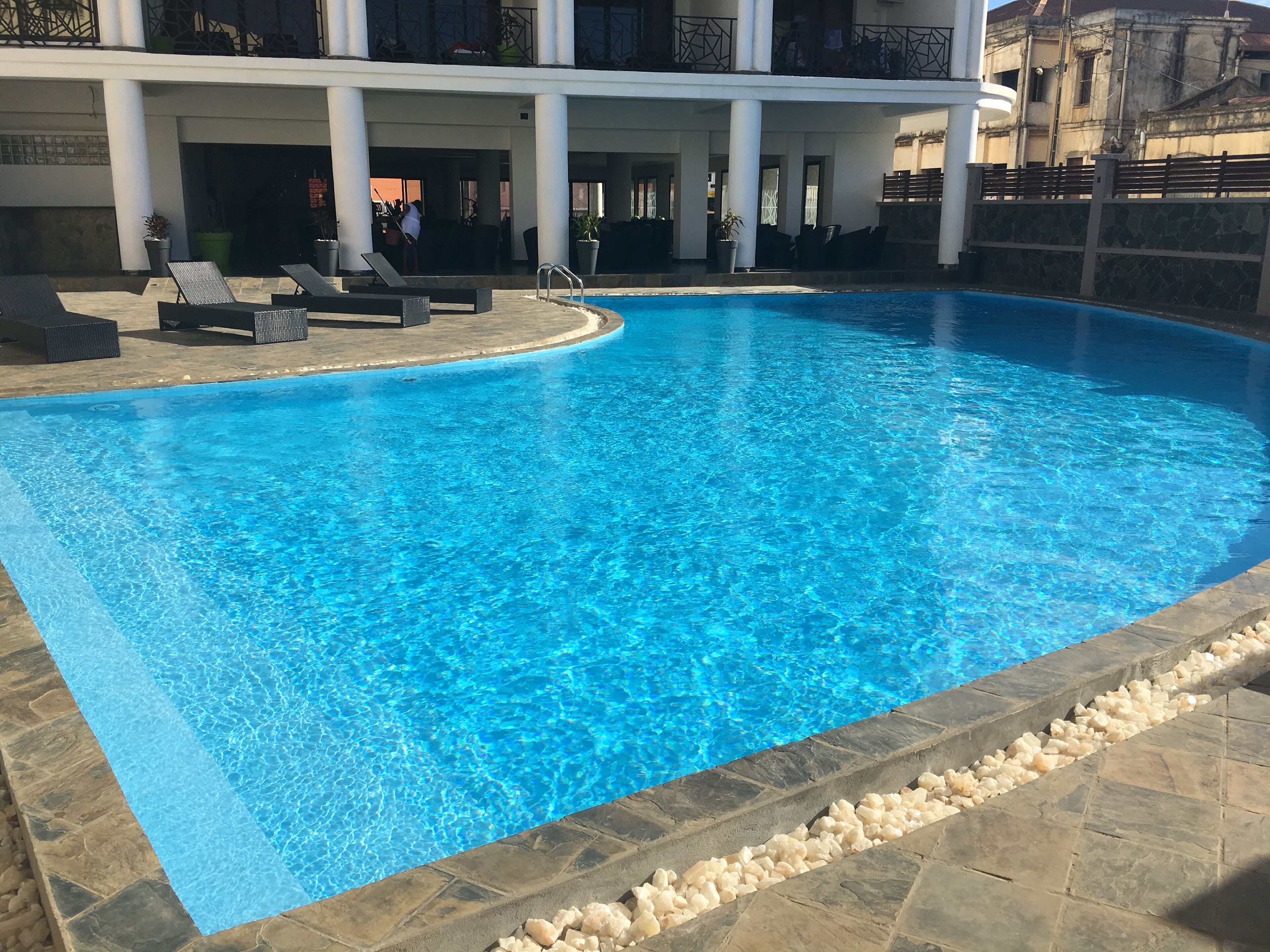 A clear blue swimming pool with lounge chairs and a stone border.