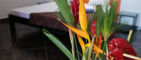 Una habitación con cama, mesita de noche y una planta con flores rojas y amarillas.