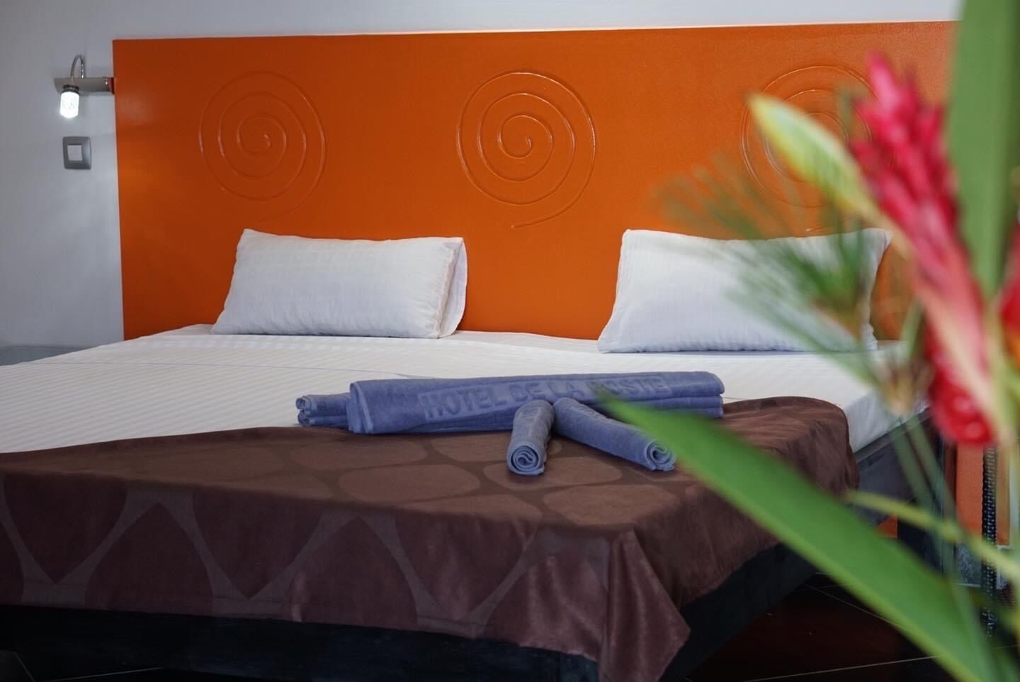 A hotel room with an orange headboard, white bedding, and a brown bedspread.