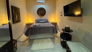 A bedroom with a bed, a TV, a ceiling fan, a wall-mounted air conditioner, and a small round table with a chair. - Mizu Villa (Chelem)