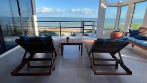 A balcony with two wooden lounge chairs, a small table, and a sofa with cushions. The balcony overlooks a beach and the ocean. - Mizu Villa (Chelem)