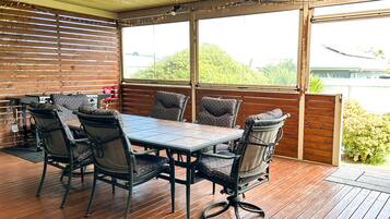Une terrasse extérieure avec une plateforme en bois, une table ronde entourée de chaises, et une vue sur la verdure et un bâtiment en arrière-plan.