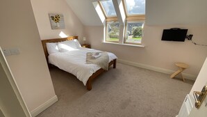 Een slaapkamer met een bed, nachtkastje, lamp, televisie aan de muur en een raam met uitzicht.