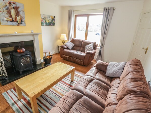 A cozy living room with a sofa, a wooden coffee table, a fireplace, and a large window with curtains.