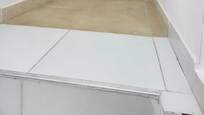 Un couloir étroit et vide, aux murs blancs et au sol carrelé.