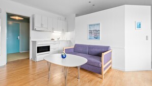 Une cuisine moderne avec des meubles blancs, un four encastré et un coin repas comprenant une table ronde et un canapé violet.