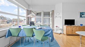 Un salon moderne avec un coin repas, de grandes fenêtres et un téléviseur.