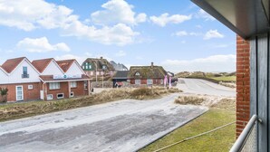 Une route côtière bordée de maisons, dont un bâtiment en briques rouges et une maison à toit de chaume.