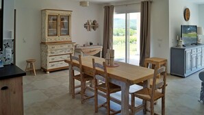 Un coin repas avec une table et des chaises en bois, un meuble avec des portes en verre et une vue sur l’extérieur grâce à une grande fenêtre.