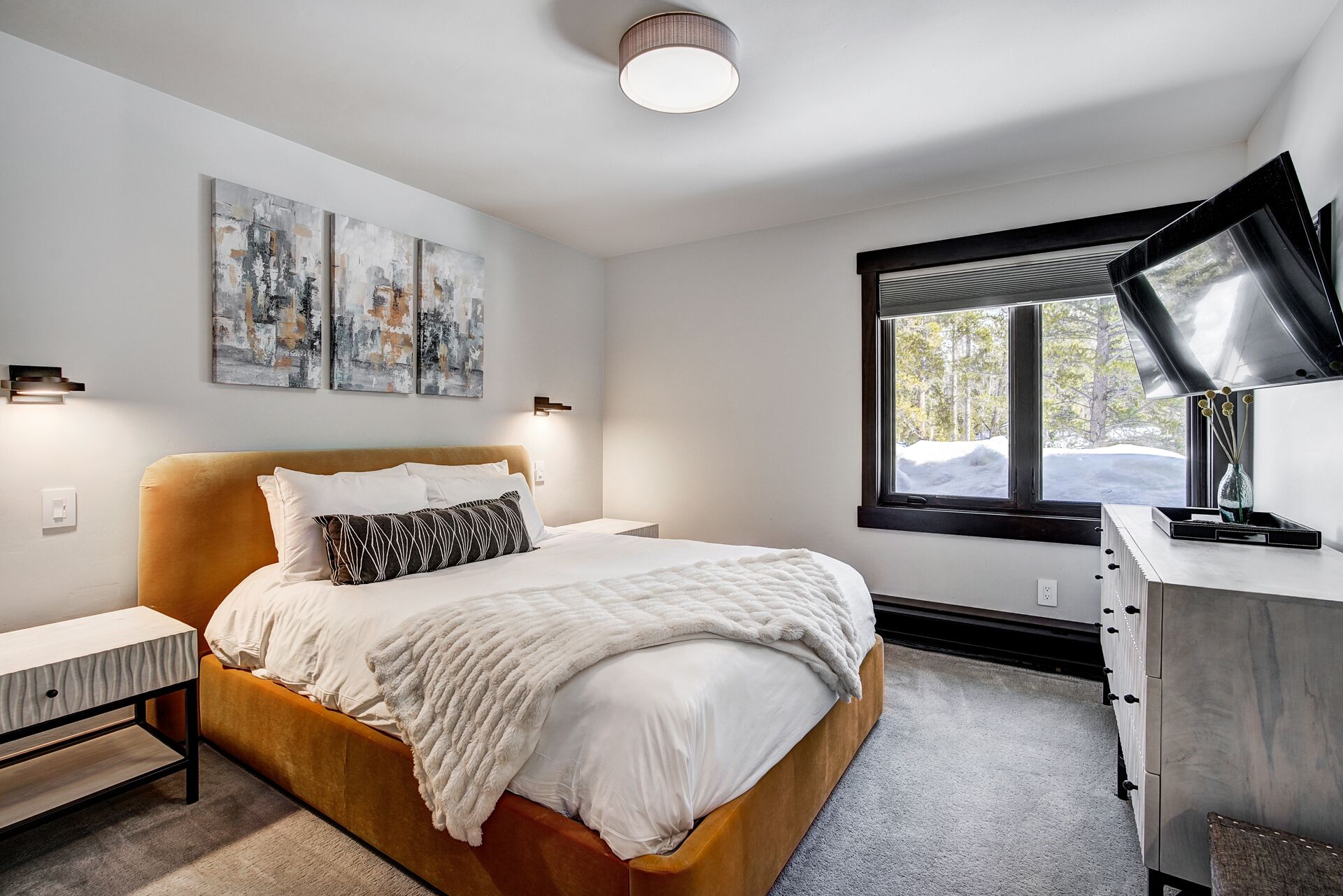 Un dormitorio moderno con cama, mesitas de noche, un escritorio y un amplio ventanal.